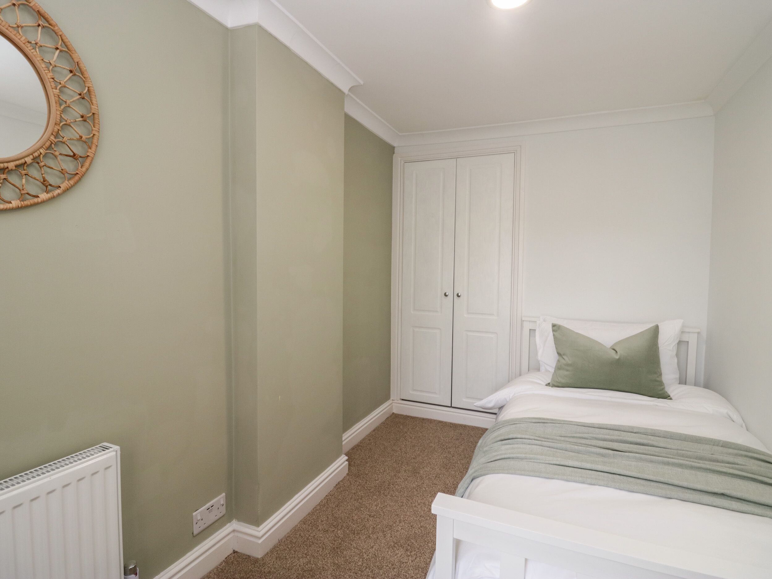 Un dormitorio con cama, armario, radiador y espejo fijado a la pared.
