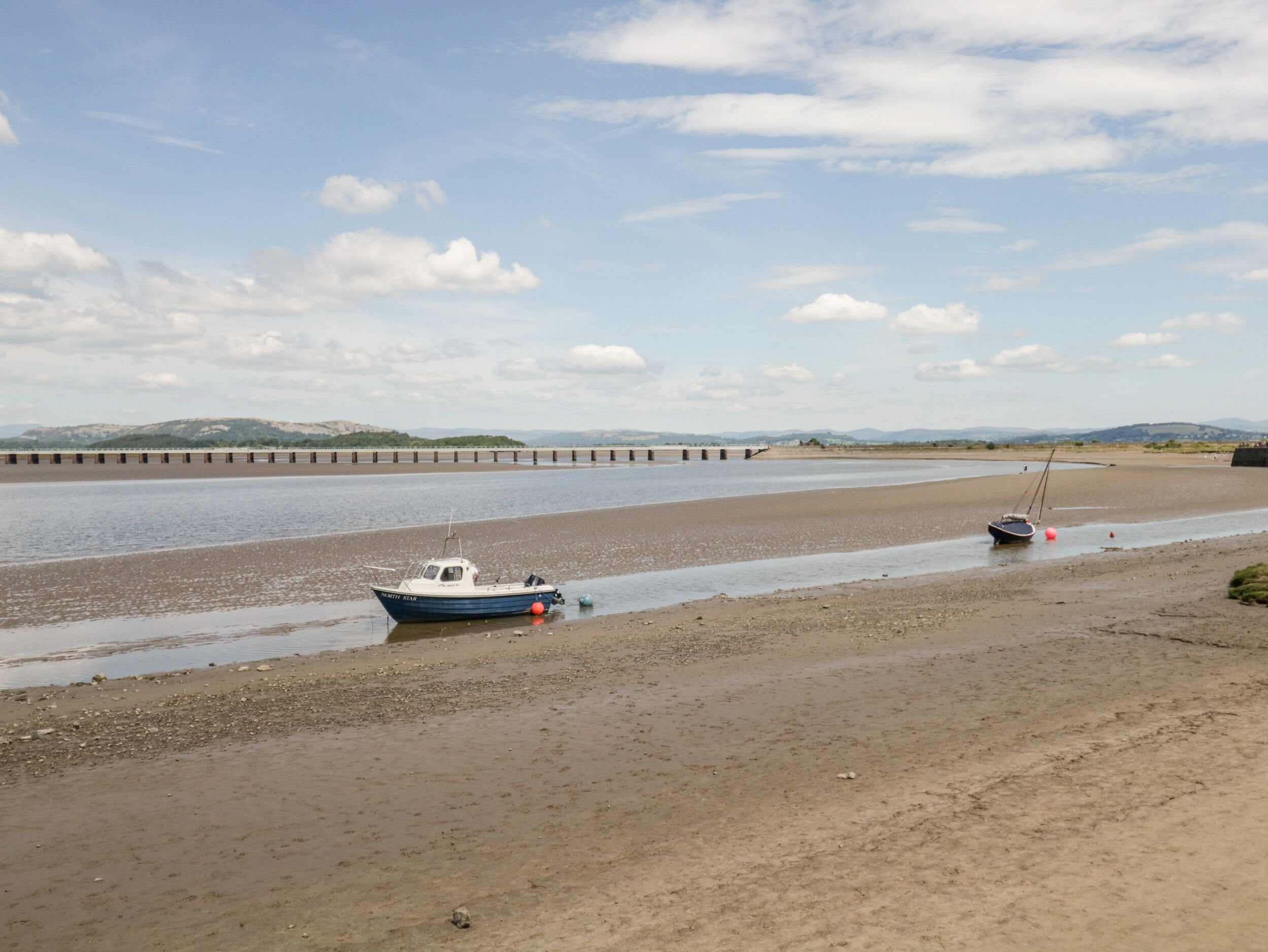 Ein Strand mit Booten, einem ruhigen Fluss und sanften Hügeln im Hintergrund.