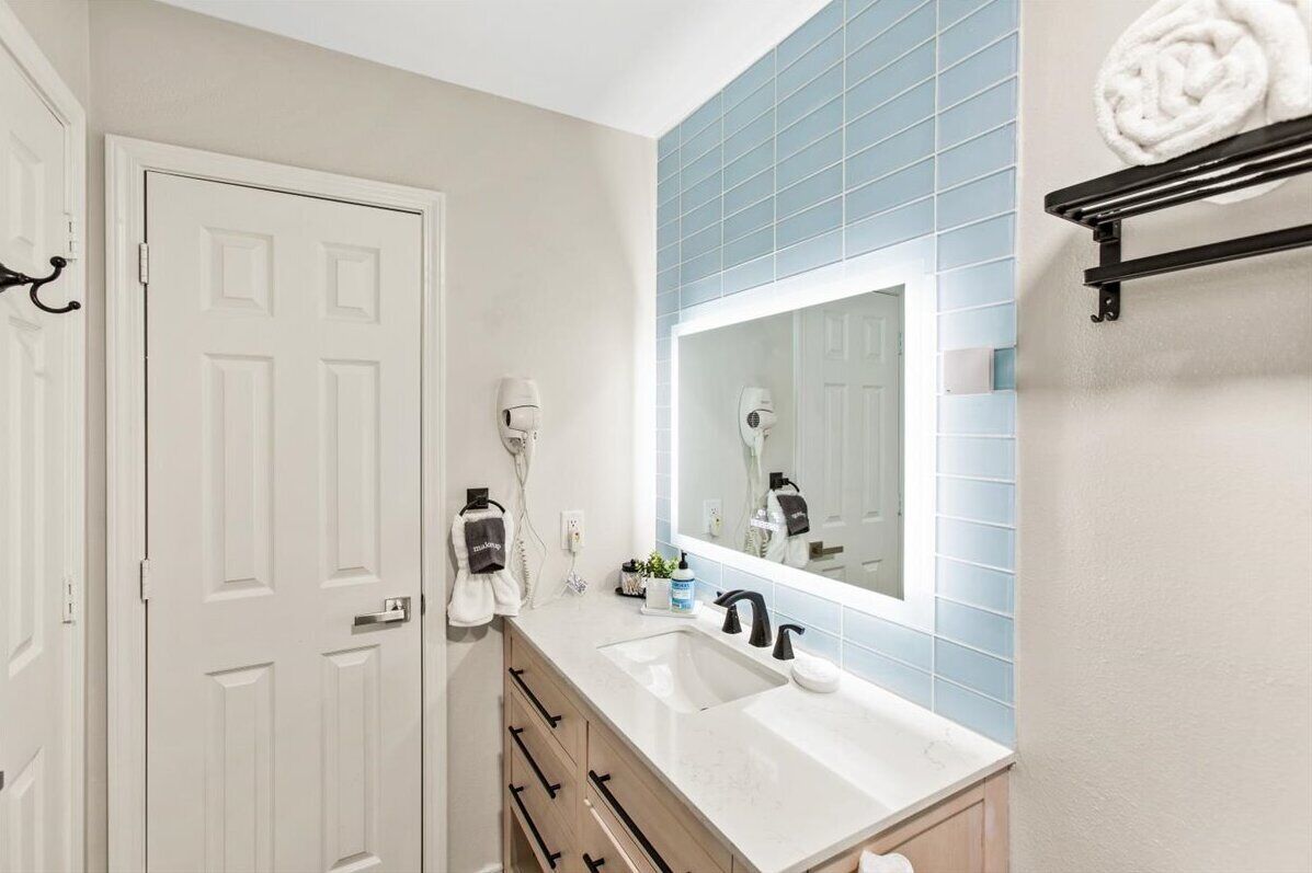 A bathroom with a white door, a sink with a mirror, and a towel rack with a towel.