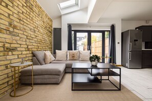 Ein modernes Wohnzimmer mit Backsteinwand, einem Ecksofa, einem runden Couchtisch und einer Küchenzeile mit Kühlschrank.