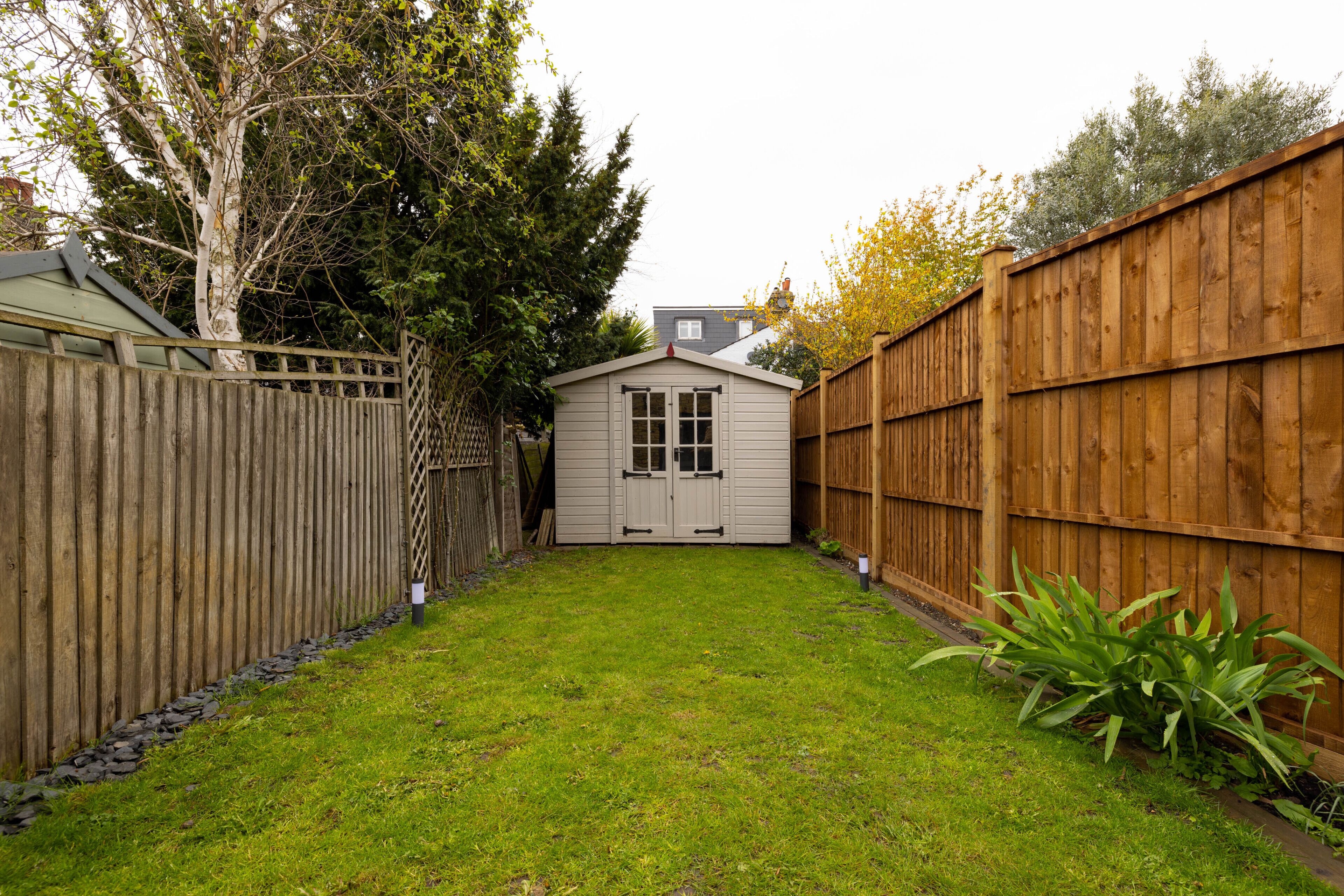 A backyard with a wooden fence, a shed, and a well-maintained lawn.