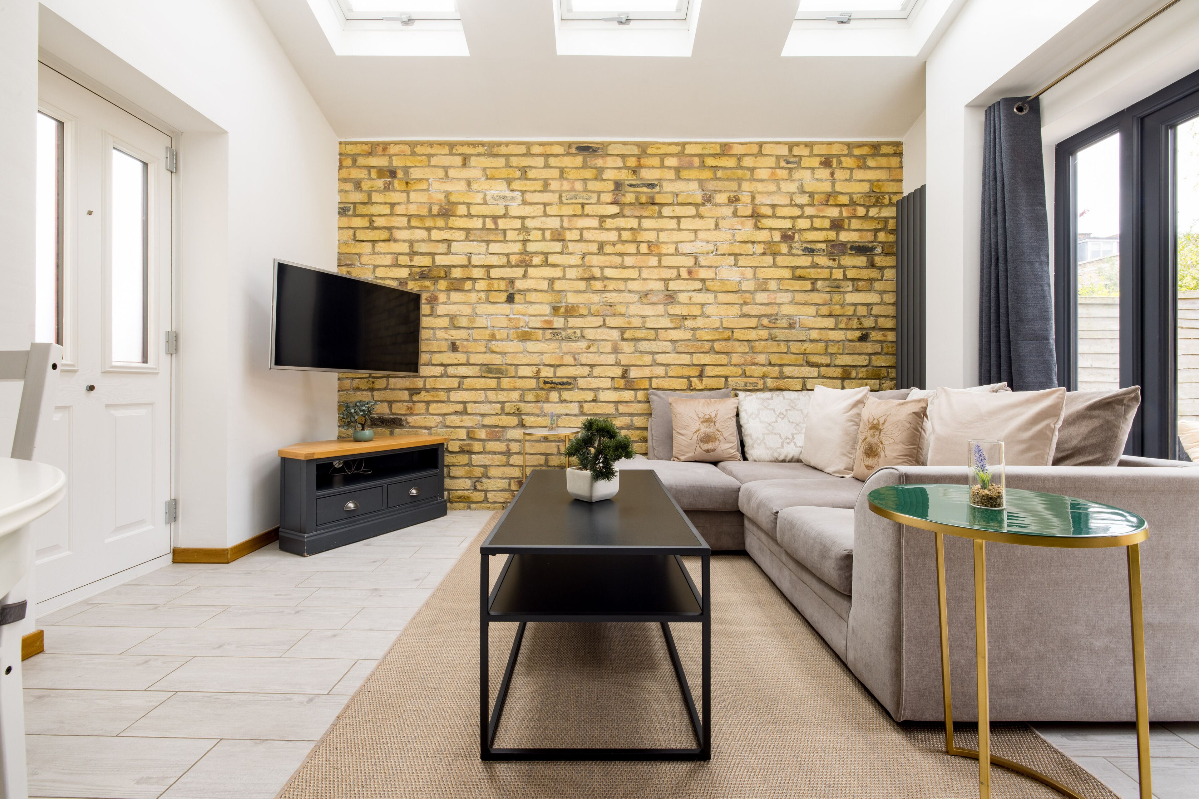 Een moderne woonkamer met een bakstenen muur, een flatscreen televisie, een bank, een salontafel en een klein bijzettafeltje.