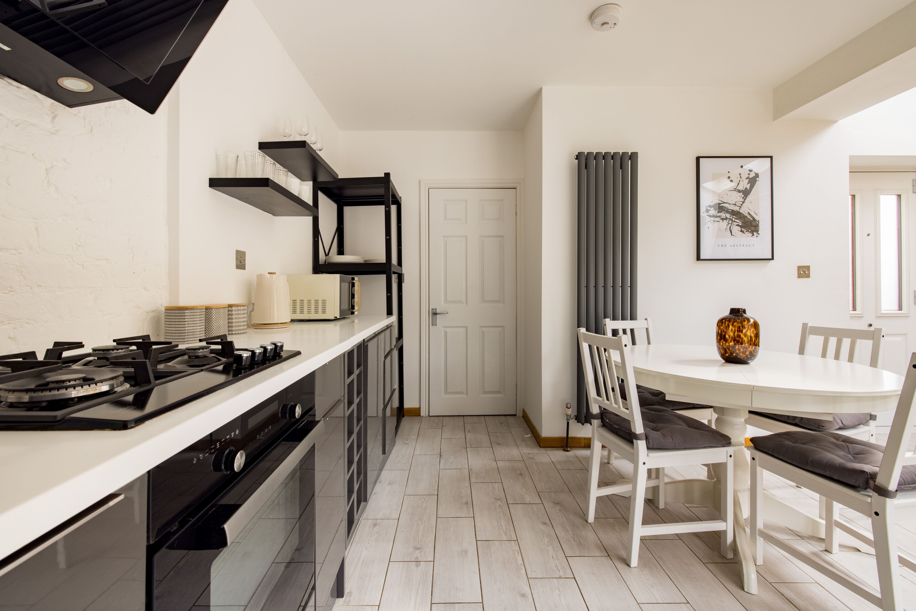 A modern kitchen with a white countertop, black appliances, and a dining area with white chairs and a table.