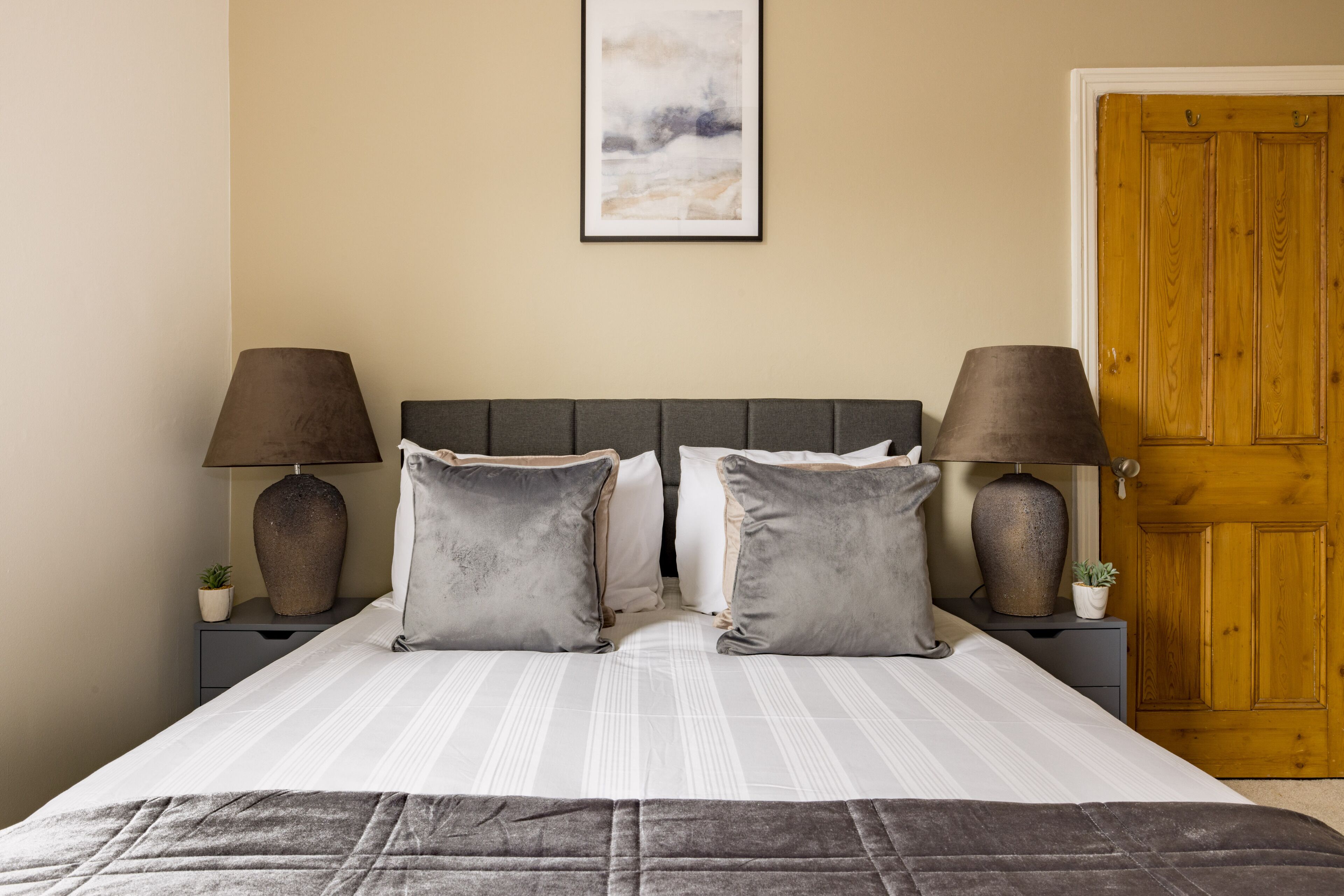 A neatly made bed with a striped bedspread, two bedside lamps, and a framed picture on the wall.