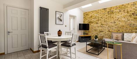 A modern living room with a dining area, a brick wall, and a flat-screen TV.