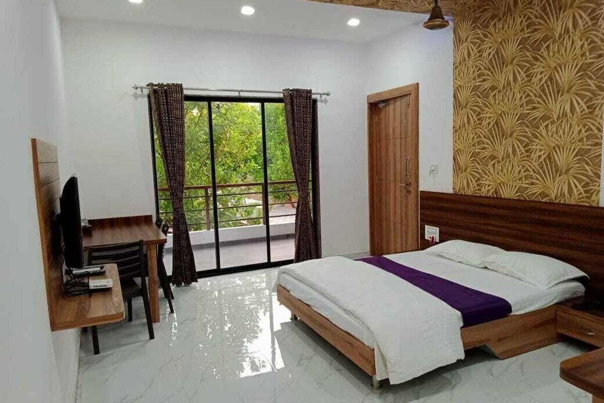 A bedroom with a bed, a desk, a television, and a window with curtains.