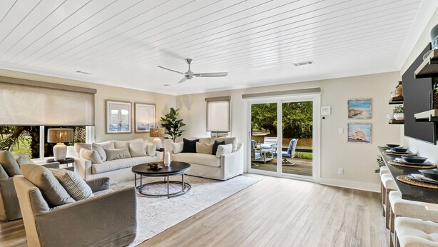 A spacious living room with a large sofa, a coffee table, and a ceiling fan. There is a sliding glass door leading to an outdoor patio area. - Recently updated Palmetto Dunes villa with fairway views and community pools. (Hilton Head Island)