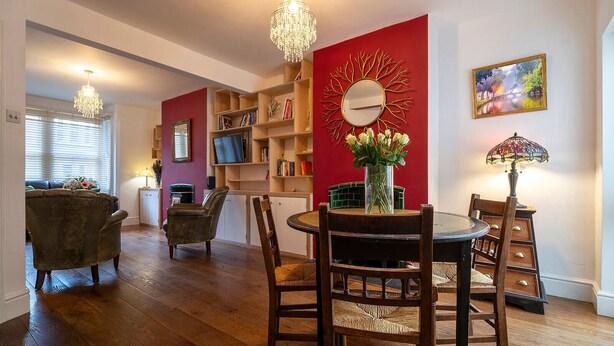 A dining area with a round table, chairs, a chandelier, a red accent wall, and a bookshelf. - Charming Victorian Home - Discover the splendor of Oxford's City Spires (Oxford)