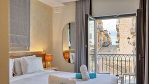 Una habitación de hotel con cama, espejo y balcón con vistas a la calle y edificios.