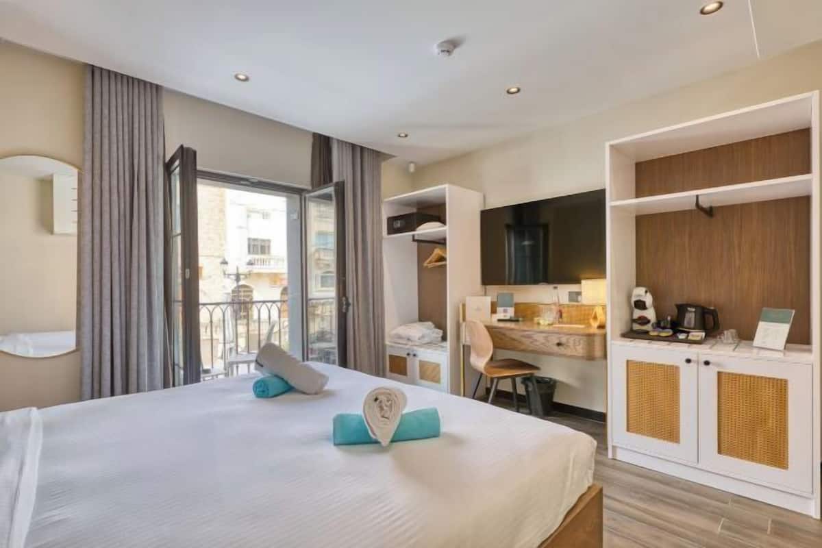 Habitación de hotel con cama, escritorio, armario y balcón.