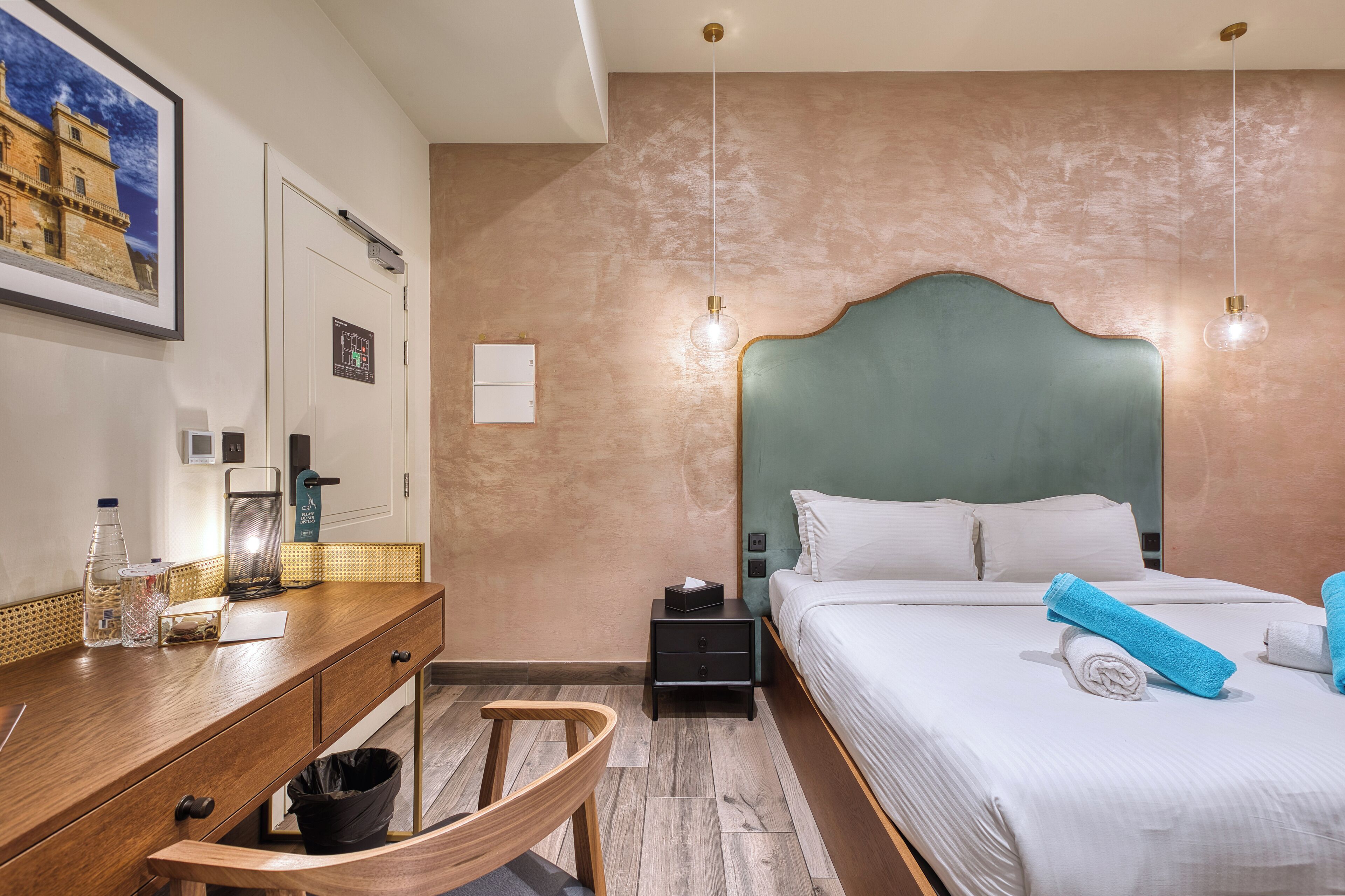 Habitación de hotel con un escritorio de madera, una cama con ropa de cama blanca y vista a un edificio a través del ventanal.