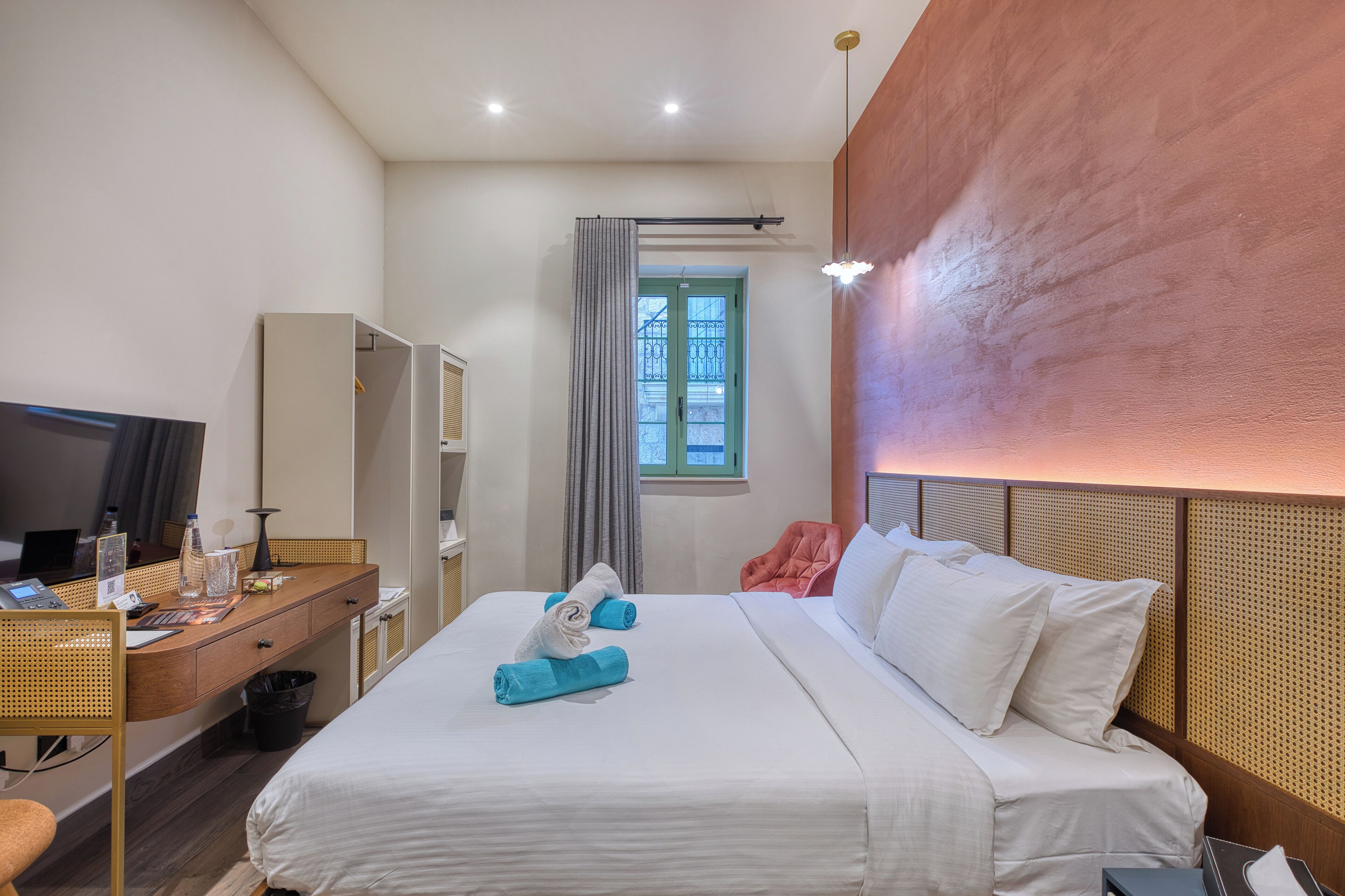 Habitación de hotel con cama, escritorio con computadora, silla, televisor y ventana con cortinas.