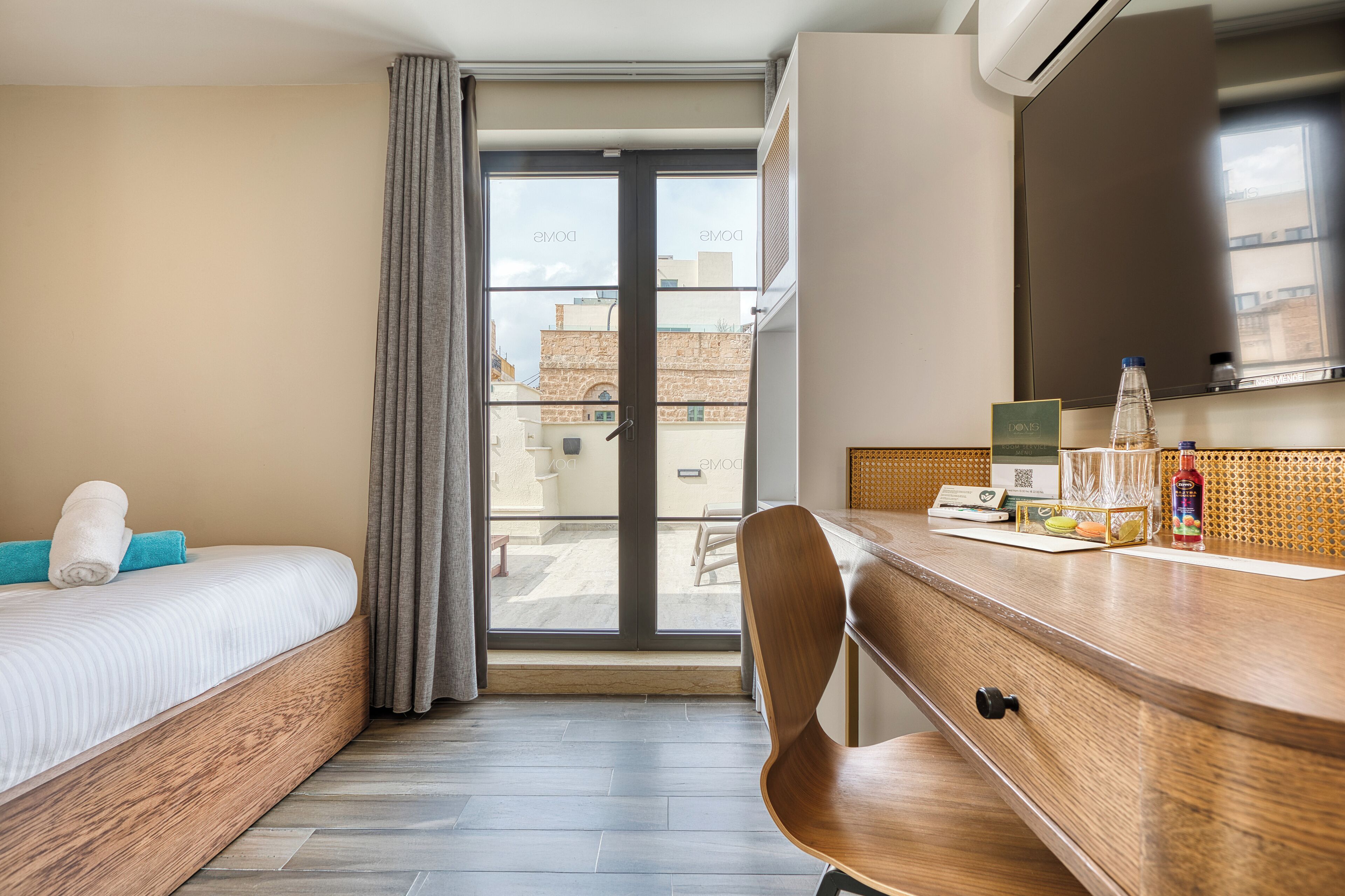 Hotelkamer met een bed, bureau, stoel, raam met uitzicht op gebouwen en een deur.