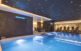 A modern indoor pool with a starry ceiling, lounge chairs, and a 'No Diving' sign.