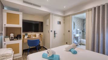 A hotel room with a bed, a desk, a chair, and a shower area.