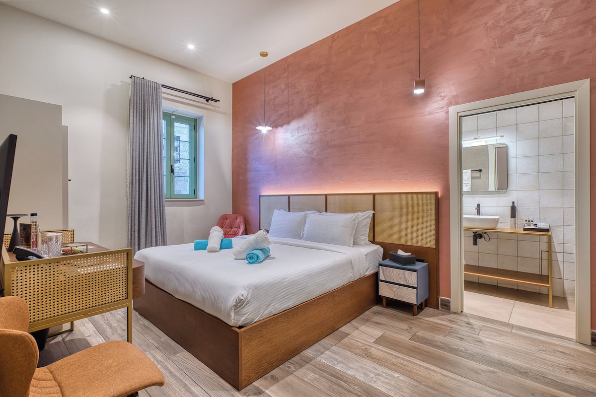 Una habitación de hotel moderna con una cama grande, un escritorio con una computadora, una silla y un baño con lavamanos y espejo.