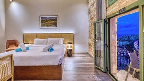 Habitación de hotel con cama, una silla, mesita de noche y balcón con vistas a la ciudad.