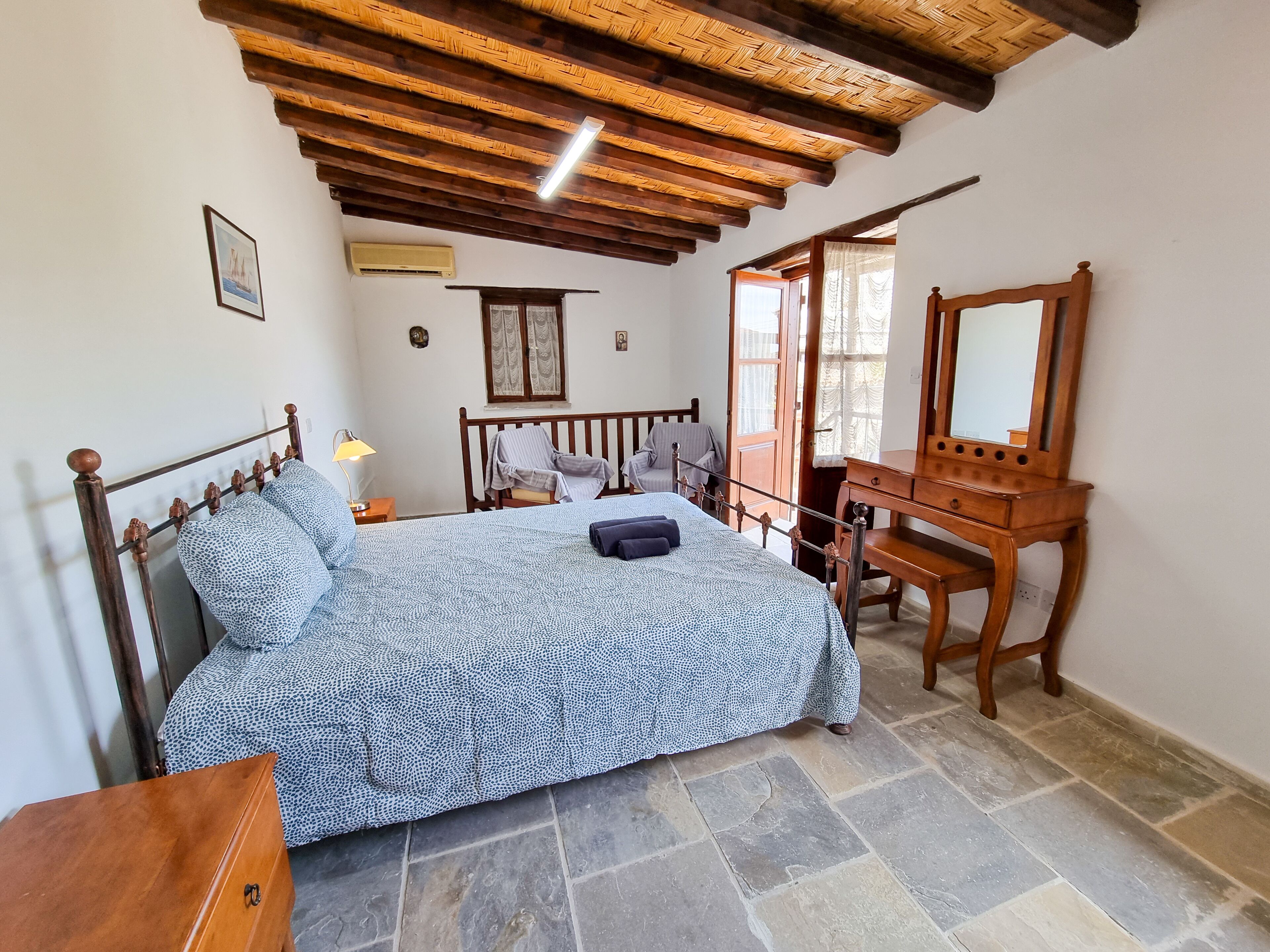 A bedroom with a bed, a wooden dresser, a mirror, and a stone floor.