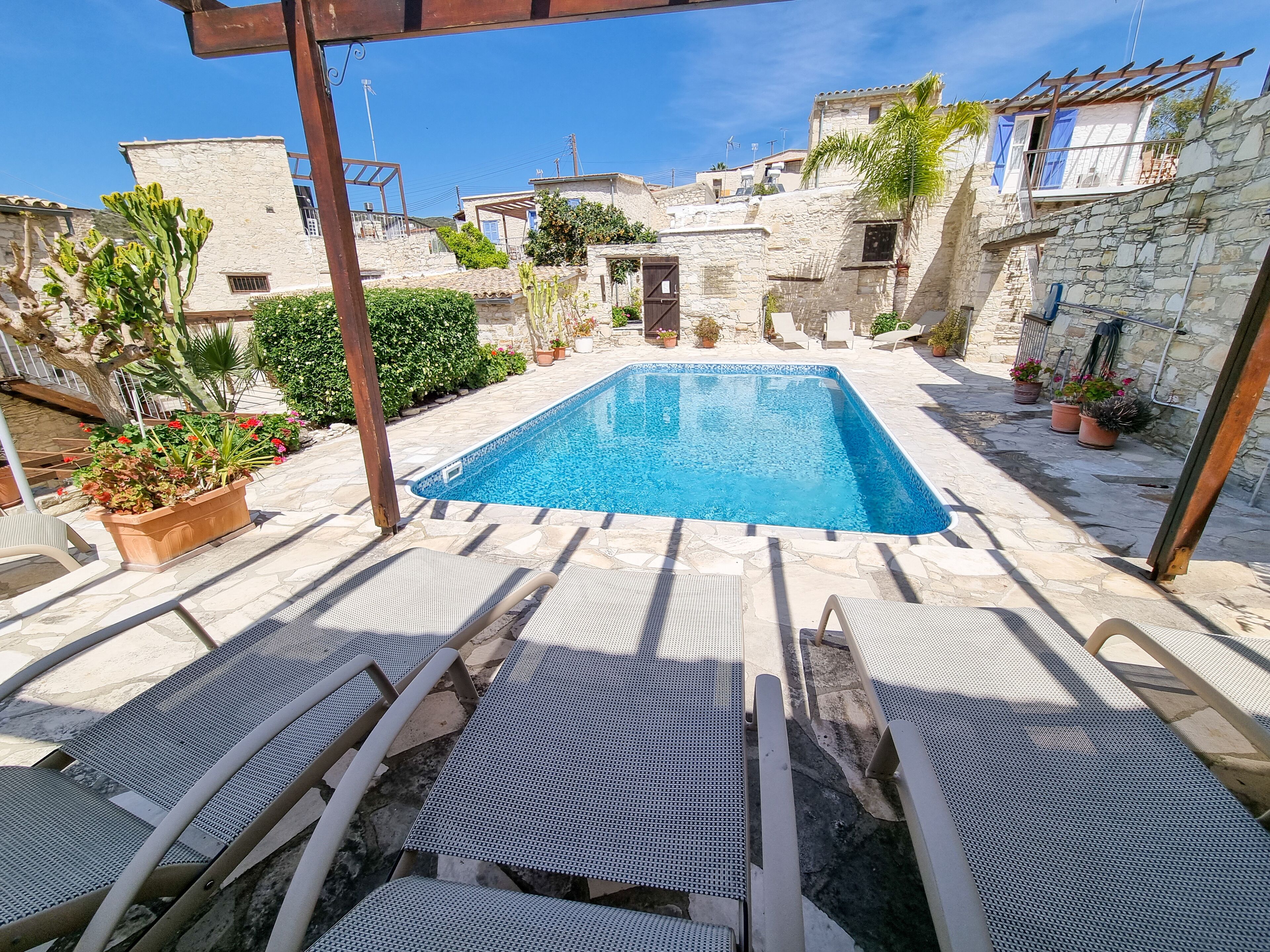 A rooftop pool with stone buildings, potted plants, and lounge chairs.