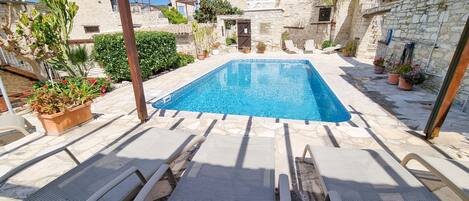 A rooftop pool with stone buildings, potted plants, and lounge chairs.