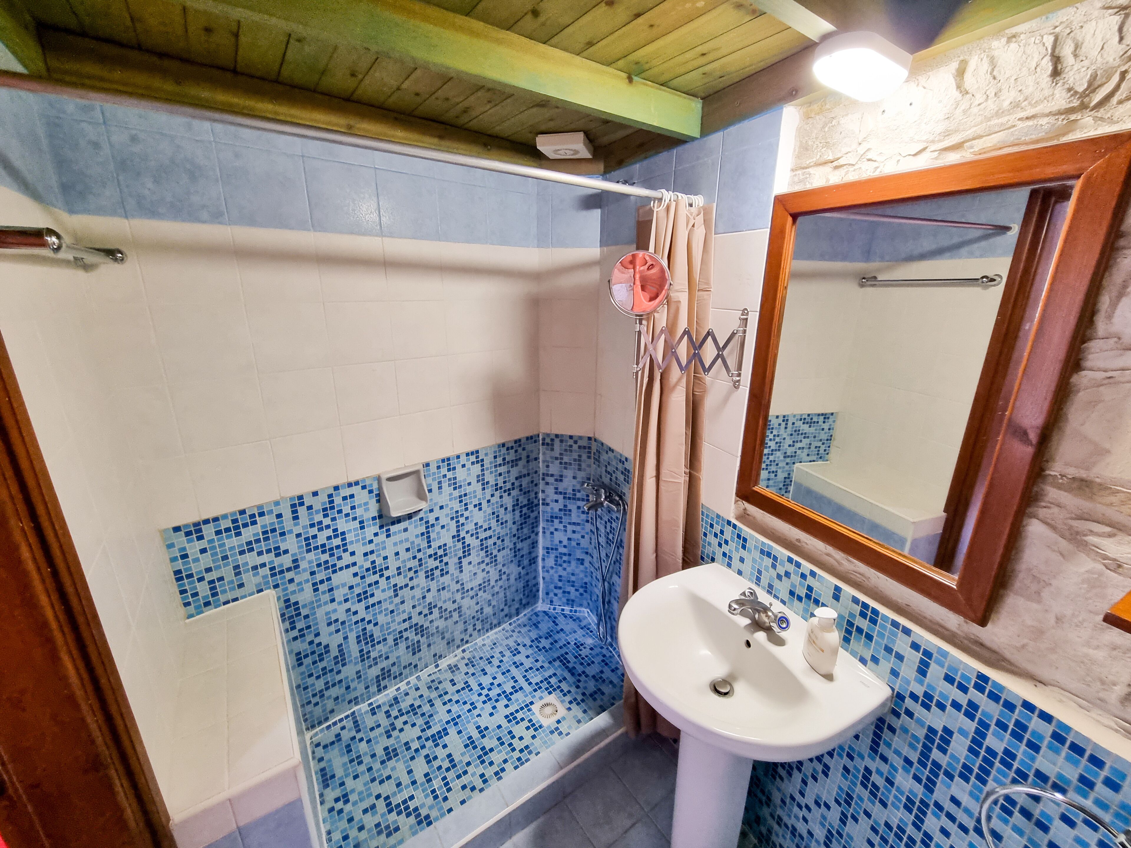 Ein Badezimmer mit einer blauen Duschkabine aus Mosaikfliesen, einem weißen Waschbecken und einer Holzbalkendecke.