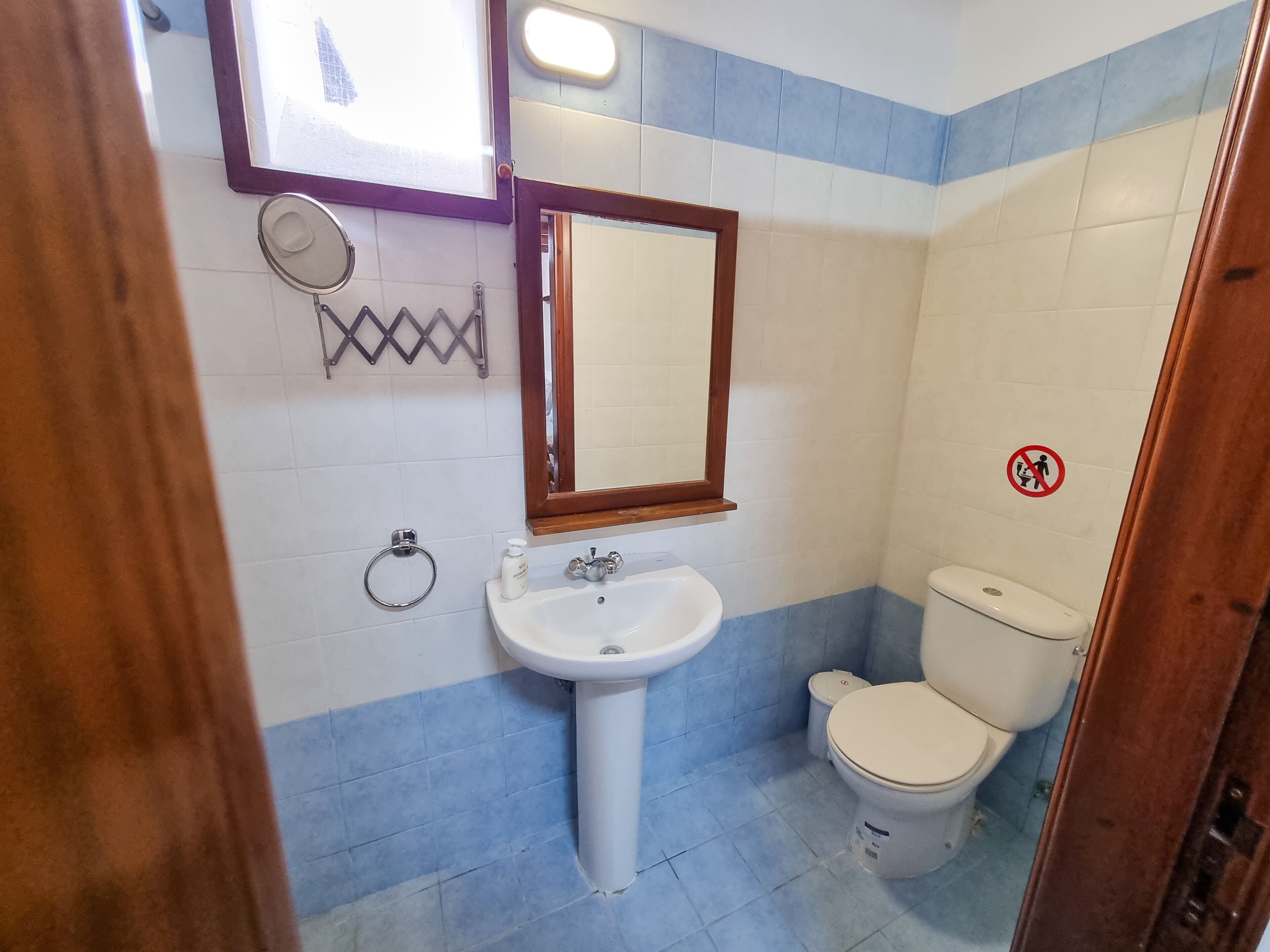 Ein Badezimmer mit weißem Waschbecken, einem Spiegel, einer Toilette und einem Handtuchhalter.