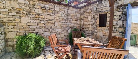 An outdoor patio with stone walls, wooden furniture, and a pergola structure.