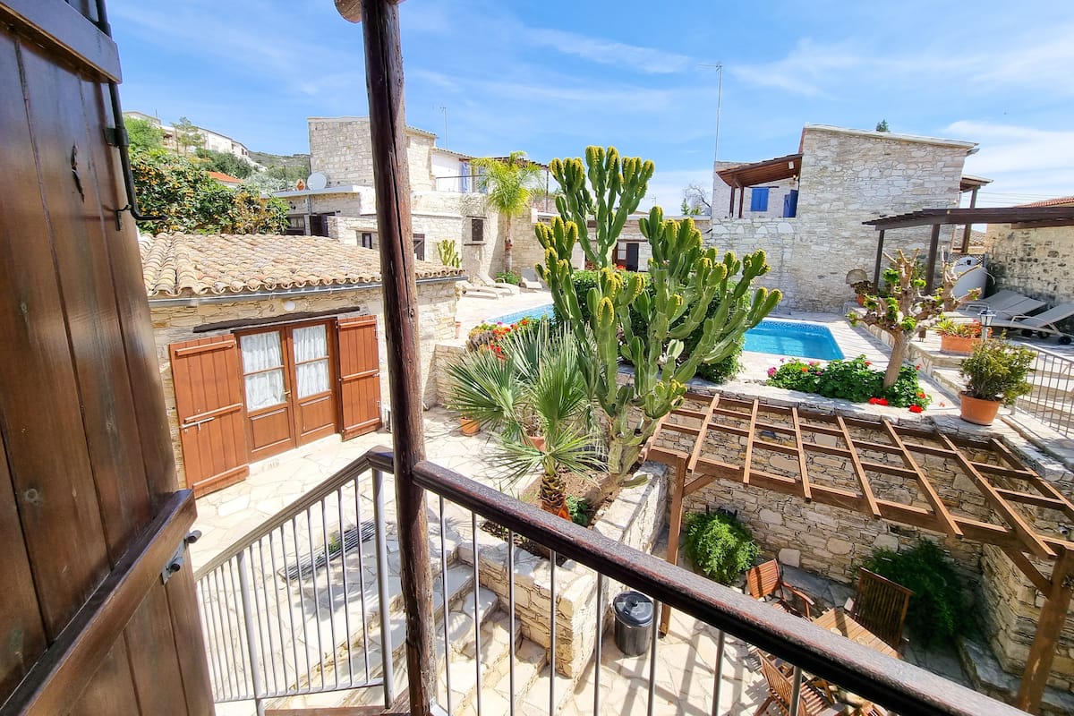 A balcony with a view of a pool, stone buildings, and cacti.