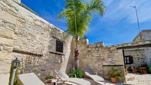 Un patio de piedra con sillones de descanso, una palmera y un muro de piedra.