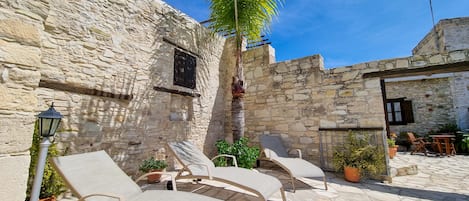 Un patio de piedra con sillones de descanso, una palmera y un muro de piedra.