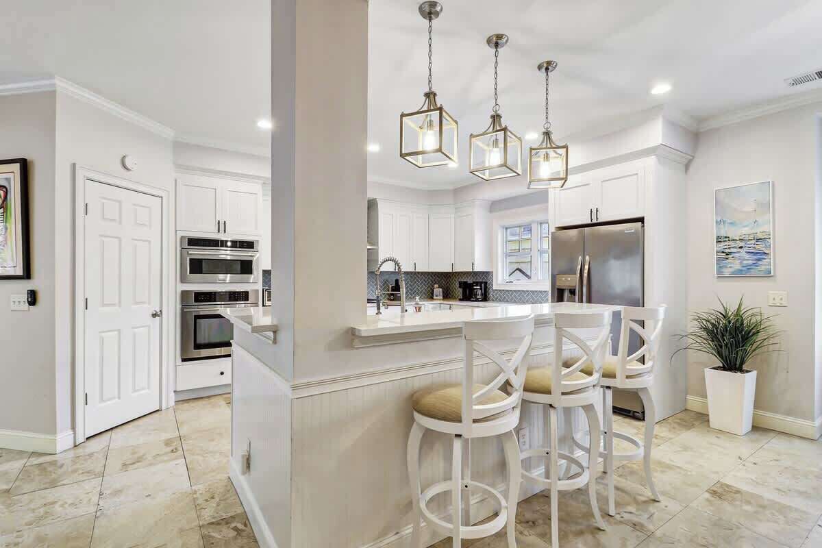 A modern kitchen with white cabinetry, a central island, bar stools, and pendant lighting.