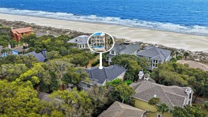 An aerial view of a coastal residential area with houses, a beach, and a large circular structure.