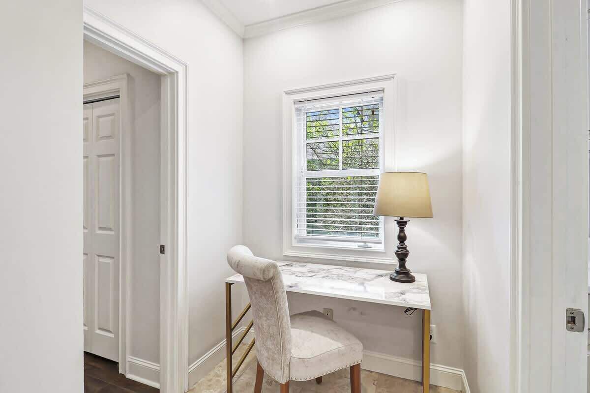 A study with a desk, chair, lamp, and window with blinds.