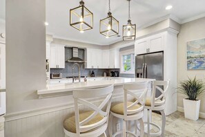 Una cocina moderna con armarios blancos, una isla central con taburetes altos y luminarias colgantes.