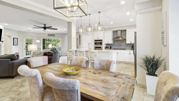 A modern kitchen with white cabinetry, a wooden dining table, and pendant lighting. - Massive Luxury Beach Home Private Pool Hilton Head (Hilton Head Island)