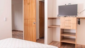 Un dormitorio con cama, un armario de madera con el número 301, un televisor sobre un mueble bajo y un escritorio con cajones.