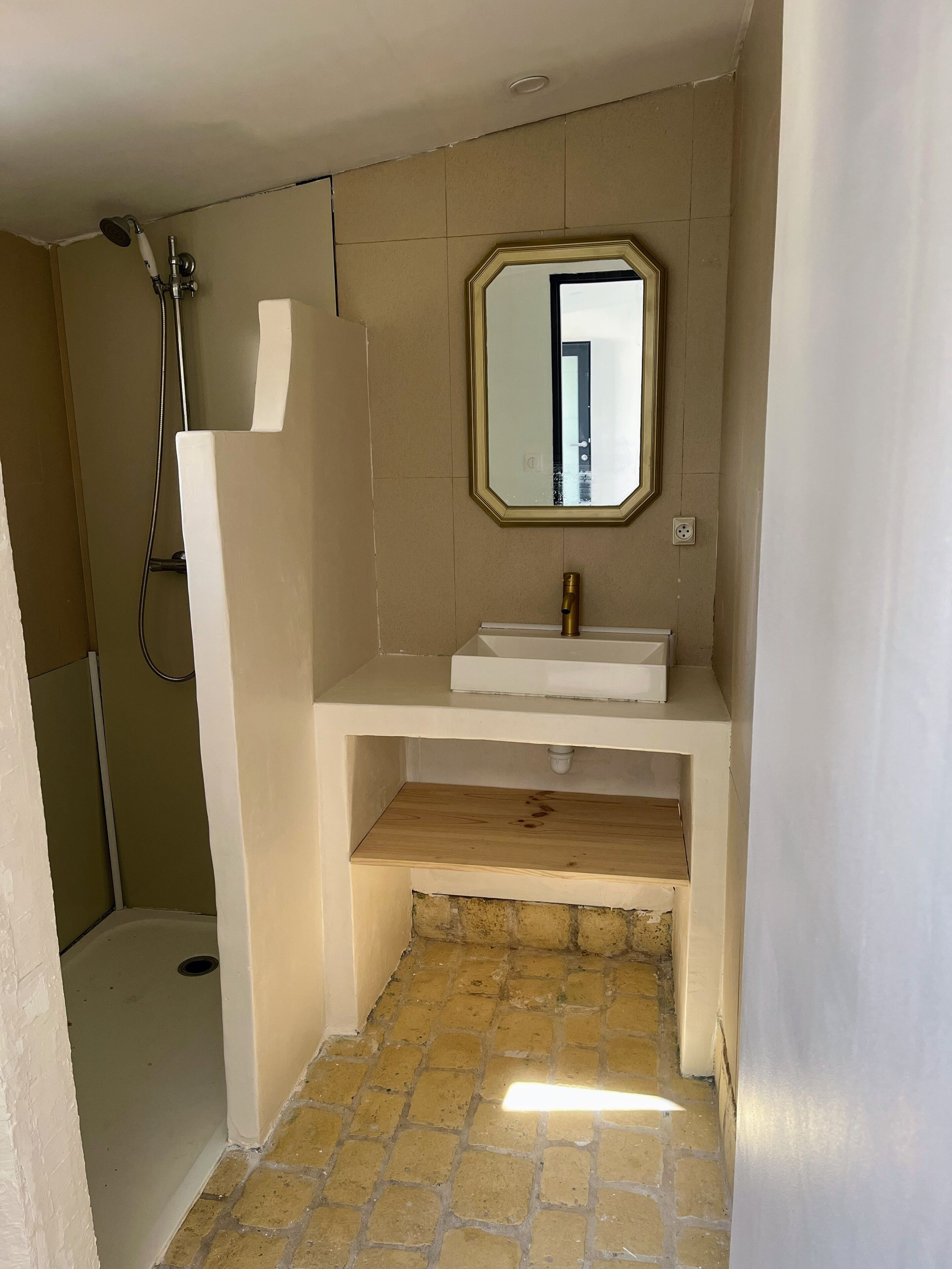 Een badkamer met een douche, wastafel, spiegel en een houten plank.