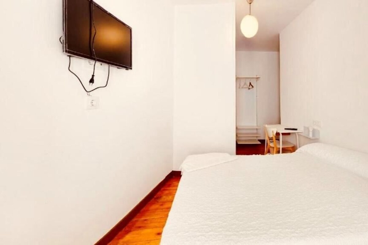 Een slaapkamer met een bed, een aan de muur bevestigde televisie, een bureau en een stoel.