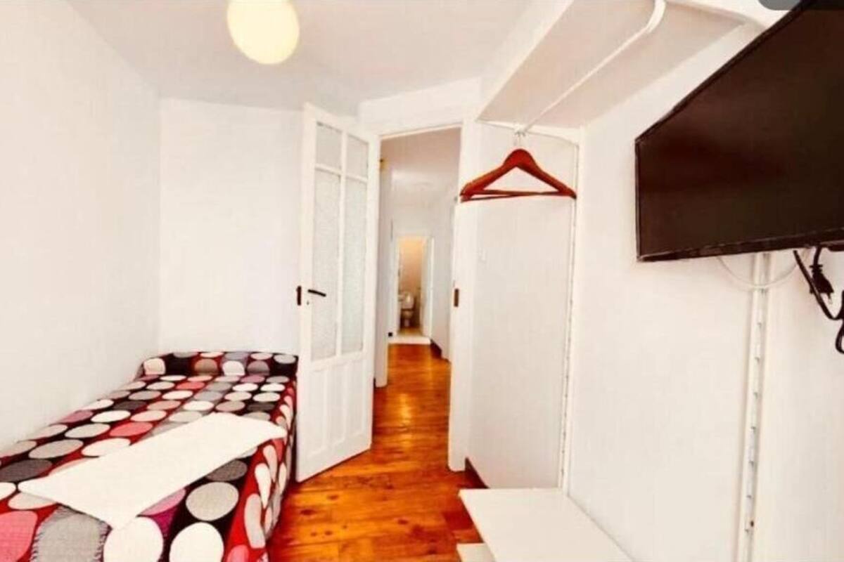 En smal hall med en säng på vänster sida, en tv på höger sida och en dörr längst ner.
