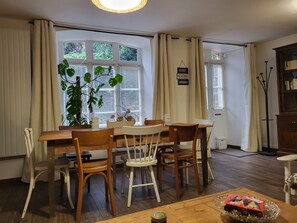 A dining area with a wooden table and chairs, a potted plant, and a sign on the wall.