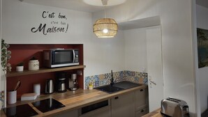 A compact kitchen with a microwave, coffee maker, and toaster. A decorative sign on the wall reads "C'est bon, c'est fait Maison!" A hanging light fixture and a tiled backsplash are also visible. - Maison Médiévale au Cœur de la Vieille Ville de Dinan (Dinan)