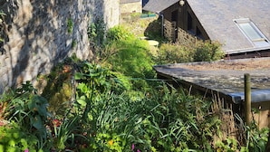 A traditional stone building with a sloped roof, surrounded by lush greenery and a clear blue sky. - Maison Médiévale au Cœur de la Vieille Ville de Dinan (Dinan)
