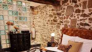 A bedroom with a stone wall, a bed with white bedding, a bedside table with a lamp, and a tray with a cup and croissant. - Maison Médiévale au Cœur de la Vieille Ville de Dinan (Dinan)