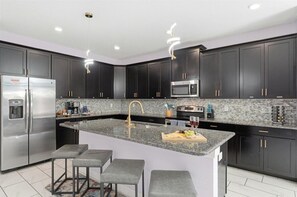 A modern kitchen with dark cabinets, stainless steel appliances, a granite countertop, and a central island with bar stools.