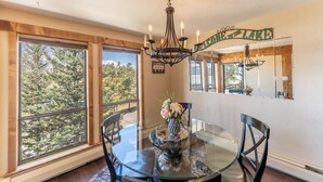 A dining area with a round glass table, black chairs, a chandelier, a vase with flowers, and a 'Welcome to Lake House' sign.