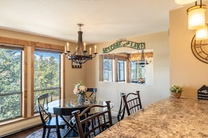 A dining area with a chandelier, a welcome sign, and a view of trees through large windows.