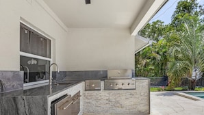 An outdoor kitchen with a marble countertop, stainless steel appliances, and a brick backsplash. - Fairview Getaway (Fort Myers)