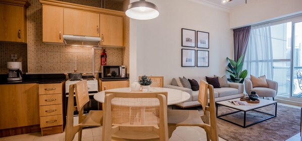 Une cuisine moderne avec des meubles en bois, un coin repas avec une table ronde et des chaises, un salon avec un canapé et une table basse, et une grande fenêtre avec des rideaux.