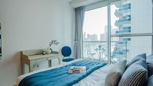 Ein modernes Hotelzimmer mit Bett, Schreibtisch, Stuhl und einem Balkon mit Blick auf die Stadt.