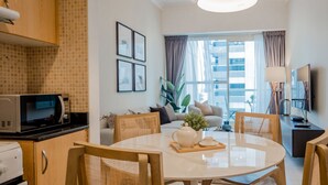 Ein modernes Wohnzimmer mit einem runden Esstisch, bequemen Sitzmöglichkeiten, einer Küchenzeile mit Mikrowelle und einem großen Fenster mit Blick auf die Stadt.